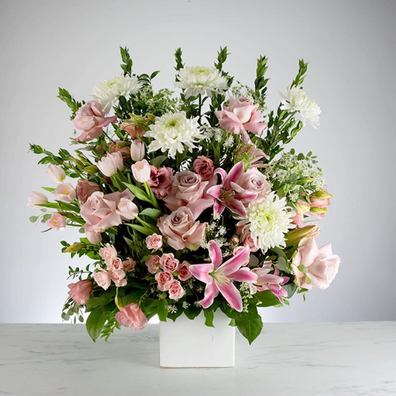 Elegant floral arrangement with pink lilies and white flowers in a white vase.