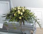 A silver casket adorned with a lush white and green floral arrangement.