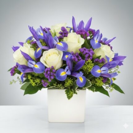 A premium floral arrangement featuring vibrant blue irises, cream-white roses, and purple statice flowers in a clean white square ceramic vase.