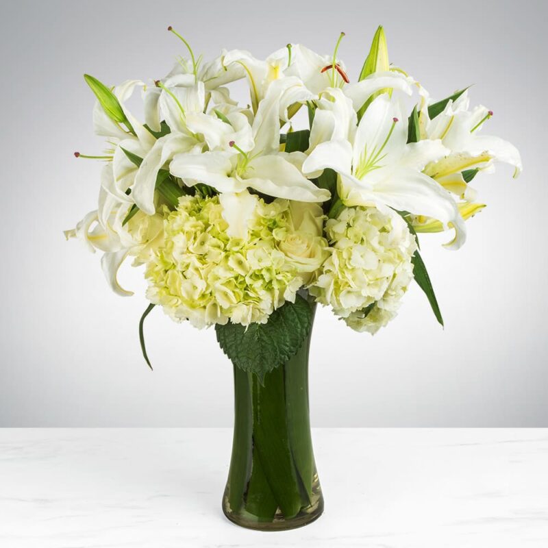 Elegant bouquet of white lilies and hydrangeas in a green vase.