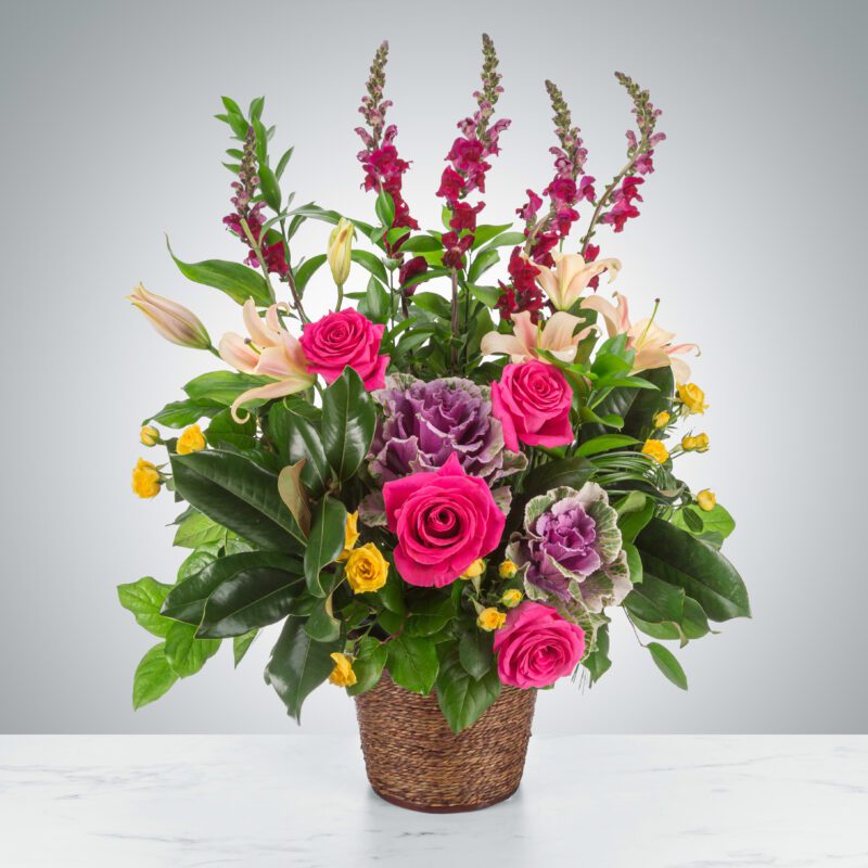 Elegant floral arrangement with pink roses and tall purple flowers in a woven basket.
