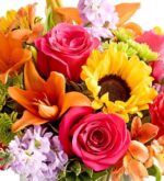 A vibrant and colorful floral bouquet featuring hot pink roses, bright orange lilies, a yellow sunflower, and light purple stock flowers.
