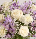 A close-up photograph of a lush floral arrangement featuring white roses, cream carnations, purple alstroemeria, and delicate baby's breath.
