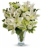 A lush "Purest Love" floral arrangement featuring white lilies, alstroemeria, carnations, and green hydrangeas in a clear glass vase.