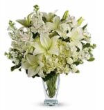 An elegant all-white floral arrangement featuring large oriental lilies, white hydrangeas, alstroemeria, and stock flowers in a clear glass pedestal vase.