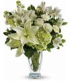 A lush and elegant floral arrangement in a clear glass vase, featuring white lilies, cream carnations, white alstroemeria, and green hydrangea accented with variegated greenery.