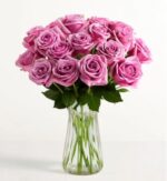 A lush bouquet of approximately two dozen premium lavender-purple roses with long green stems arranged in a clear, ribbed glass vase against a plain white background.