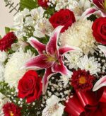 A vibrant floral arrangement featuring red roses, a pink Stargazer lily, white chrysanthemums, and delicate baby's breath, accented with a large red satin ribbon.