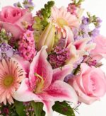 A lush and vibrant floral arrangement featuring pink Oriental lilies, light pink roses, pale pink gerbera daisies, and purple stock flowers accented with green foliage.