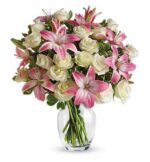 Elegant bouquet of pink stargazer lilies and cream-colored roses with green foliage in a clear glass vase