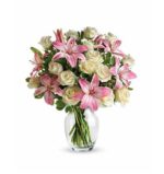 A lush bouquet of pink stargazer lilies and cream white roses in a clear glass vase, accented with green foliage.