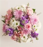 A top-down view of a lush floral bouquet featuring pink roses, purple chrysanthemums, white daisies, and purple stock flowers against a neutral cream background.