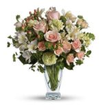 Elegant flower arrangement in a clear glass vase featuring soft pink roses, pale green carnations, white alstroemeria, and small coral hypericum berries with lush greenery