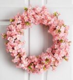Pink artificial cherry blossom wreath densely covered in full blooms, hanging on a white paneled door