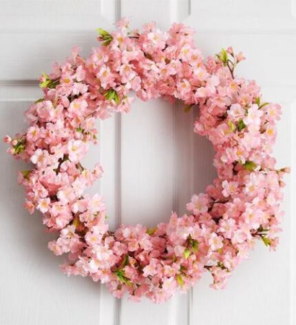 Pink artificial cherry blossom wreath densely covered in full blooms, hanging on a white paneled door