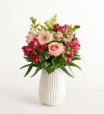 A lush floral arrangement featuring pink roses, gerbera daisies, and dark pink alstroemeria in a white textured ceramic vase.