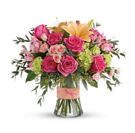 Lush bouquet of hot pink roses, pale pink spray roses, peach lilies, pink alstroemeria, and green hydrangea in a clear glass vase tied with a blush pink ribbon.