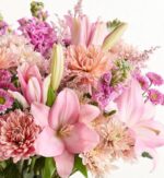 A lush and dense bouquet of various pink and peach-colored flowers, including large lilies, chrysanthemums, and snapdragons, arranged against a plain white background.