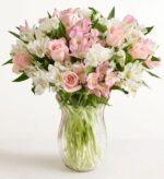 Pink roses with pink and white alstroemeria and white carnations arranged in a clear ribbed glass vase