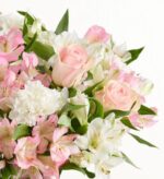 Close-up of a soft pastel bouquet featuring pale pink roses, white carnations, and pink-and-white alstroemeria flowers arranged against a white background