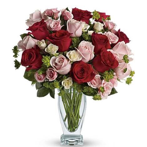 A lush round bouquet of red, pink, and white roses with green accents arranged in a clear glass vase.