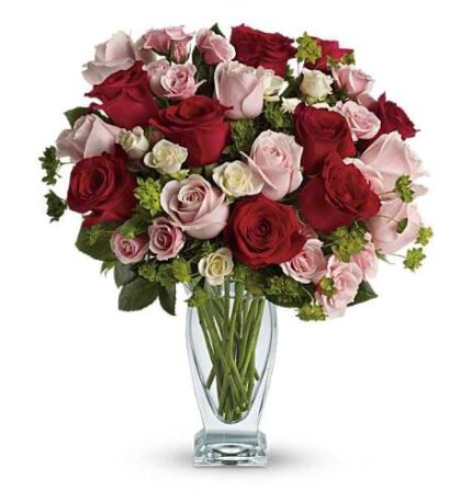 A lush round bouquet of red, pink, and white roses with green accents arranged in a clear glass vase.