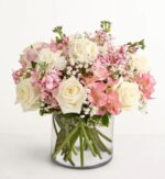 Elegant mixed flower bouquet in a clear glass vase featuring white roses, pink alstroemeria, pink stock flowers, and baby’s breath with green stems.