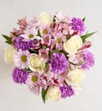 Top-down view of a round floral bouquet with cream white roses, light purple carnations, lavender daisies with green centers, and soft pink alstroemeria blooms, arranged against a white background.