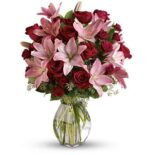 Luxurious bouquet of deep red roses and soft pink lilies with pink spray roses in a clear glass vase, accented with greenery