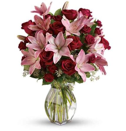Luxurious bouquet of deep red roses and soft pink lilies with pink spray roses in a clear glass vase, accented with greenery