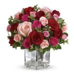 Round bouquet of red, pink, and light pink roses with eucalyptus greenery in a clear glass cube vase, viewed from above on a white background