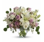 Elegant mixed flower bouquet in a clear glass vase featuring white lilies, lavender roses, white lisianthus, white stock, pink waxflower, and silver dollar eucalyptus.