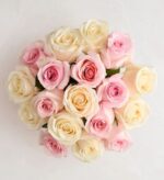 A top-down view of a dense bouquet featuring a mix of soft pink, cream, and peach-colored roses arranged in a circular cluster against a white background.