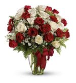 A large bouquet of long-stemmed red and white roses arranged with baby’s breath and green foliage in a clear glass vase, tied with a deep red satin ribbon.
