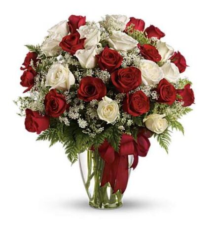 A large bouquet of long-stemmed red and white roses arranged with baby’s breath and green foliage in a clear glass vase, tied with a deep red satin ribbon.