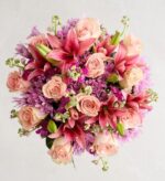 A top-down view of a lush floral bouquet featuring peach roses, vibrant pink lilies, and purple chrysanthemums.