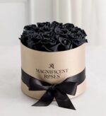 Luxury round hat box in champagne gold with a black satin ribbon, filled with a dozen preserved black roses, branded with "Magnificent Roses" logo on the front