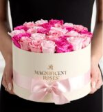 Person in black dress holding a cream round hatbox tied with a pale pink satin ribbon, filled with mixed light pink and hot pink roses.