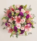 A lush and vibrant floral bouquet viewed from above, featuring pink lilies, light pink roses, purple stock flowers, and green snapdragons accented with eucalyptus leaves.