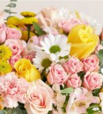 A vibrant floral arrangement featuring pink and yellow roses, white daisies, yellow chrysanthemums, and pink alstroemeria with green eucalyptus leaves.