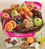 A wicker gift basket wrapped with a pink "Happy Mother’s Day" ribbon, overflowing with fresh fruit including green apples, red pears, and oranges, plus chocolate-covered pretzels, Ghirardelli chocolate squares, cookies, candied nuts, and dried fruit. A small wooden board beside it displays sliced pears, mandarin segments, almonds, and chocolate pieces.