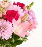 A vibrant floral arrangement featuring pink lilies, hot pink roses, and light pink chrysanthemums with green foliage against a plain white background.