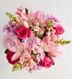 A top-down view of a vibrant floral bouquet featuring pink lilies, hot pink roses, light purple chrysanthemums, and peach snapdragons against a white marble background.