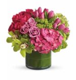 Round floral arrangement in a short green glass vase, featuring hot pink roses, magenta tulips, pink hydrangeas, green cymbidium orchids, and lime green hydrangeas with textured green accents.