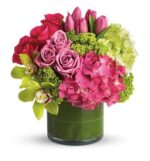 Make a statement with the New Sensations Deluxe bouquet. This luxurious arrangement bursts with hot pink roses, magenta tulips, and soft pink hydrangeas, accented by striking green cymbidium orchids and lime hydrangeas for a fresh, modern contrast. Designed low and full in a sleek leaf-lined glass vase, it brings instant energy and elegance to any space. Perfect for birthdays, congratulations, or just because. Key details: Style: Round, compact, and high-impact Flowers: Roses, tulips, hydrangeas, cymbidium orchids Palette: Hot pink, magenta, lime green Vase: Short green glass cylinder with leaf wrap Occasions: Birthday, thank you, new baby, new home