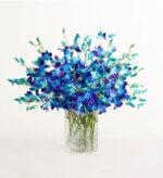 Lush bouquet of vibrant blue and purple dendrobium orchids with green stems, arranged in a clear textured glass cylinder vase on a white background.