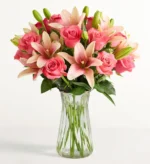 A lush bouquet of vibrant pink roses and light pink Asiatic lilies arranged in a clear fluted glass vase against a white background.