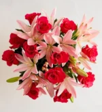 A top-down view of a vibrant floral arrangement featuring bright pink roses and soft pink lilies set against a clean white background.