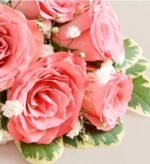 Close-up of a bouquet featuring soft coral-pink spray roses, small white baby’s breath flowers, and variegated green leaves with cream edges.