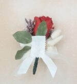 Preserved red rose boutonniere with green leaves, dried lavender sprigs, white bunny tail accents, and a white satin ribbon bow, wrapped with dark green floral tape.